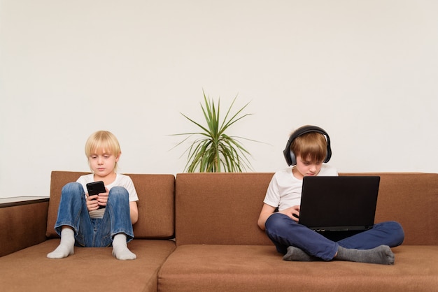 Adolescente due che si siede sul sofà con il telefono e il computer portatile. Concetto di problema di comunicazione dei bambini