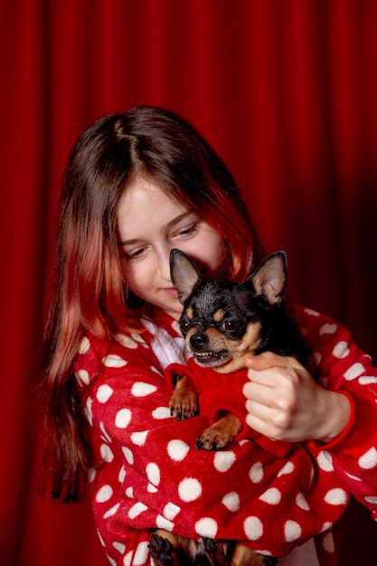 Adolescente e un chihuahua vestito con un maglione rosso per cani a casa su uno sfondo rosso.