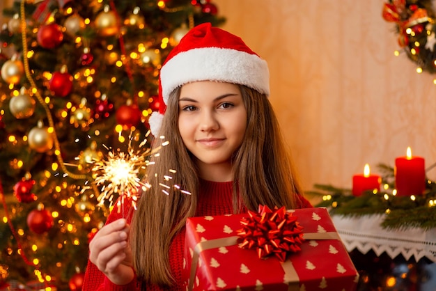 Adolescente felice con fuoco presente e bengala nella stanza decorata al concetto di celebrazione di Natale di Natale