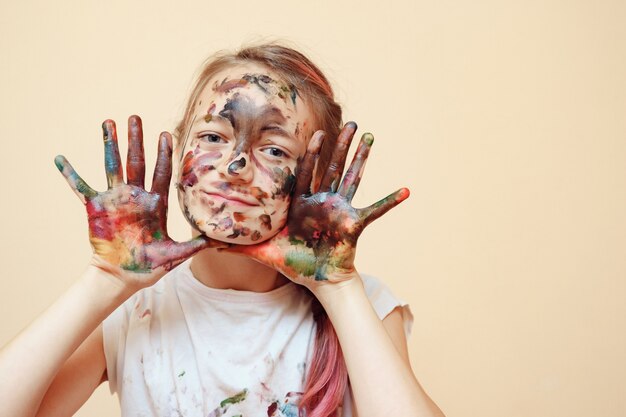 Adolescente felice con il viso e le mani in vernici colorate che sorride alla telecamera