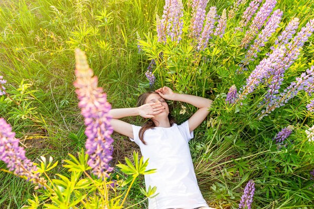 Adolescente felice sorridente all'aperto Bella giovane donna adolescente che riposa sdraiato sul campo estivo con fiori selvatici in fiore sfondo verde Bambino felice libero che si rilassa e si gode la natura