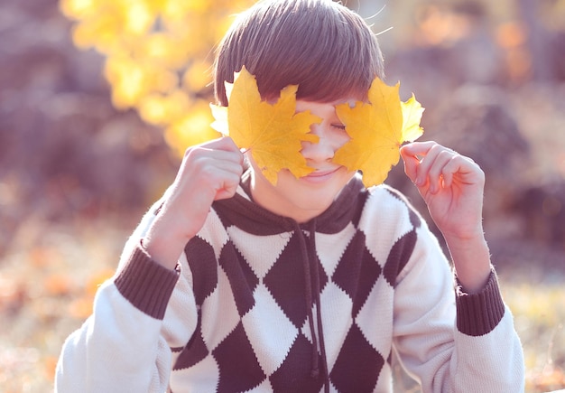 Adolescente felice sorridente di 12-14 anni che gioca con le foglie gialle nel parco all'aperto. Stagione autunnale