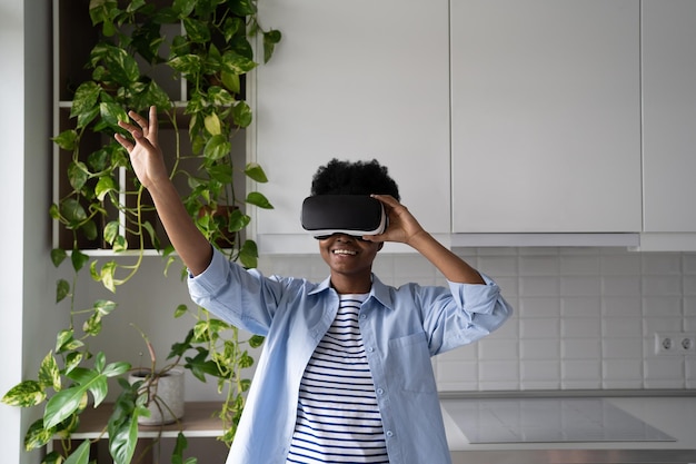 Adolescente impressionato della donna afroamericana con la cuffia avricolare di realtà virtuale di prova alzata della mano