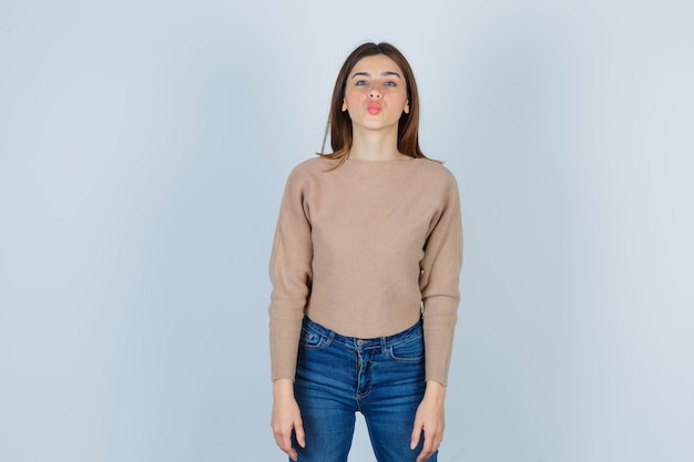 Adolescente in maglione, jeans che imbronciano le labbra e sembrano seducenti, vista frontale.