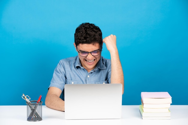 Adolescente ispanico felice che celebra buone notizie o risultati davanti al computer portatile