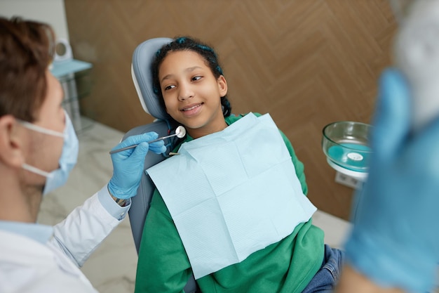 Adolescente nero seduto nella poltrona del dentista durante il controllo dei denti in clinica