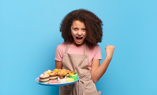 Adolescente piuttosto afro che grida in modo aggressivo con un'espressione arrabbiata o con i pugni chiusi celebrando il successo