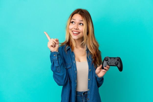 Adolescente ragazza bionda che gioca con un controller per videogiochi su un muro isolato con l'intenzione di realizzare la soluzione mentre si solleva un dito