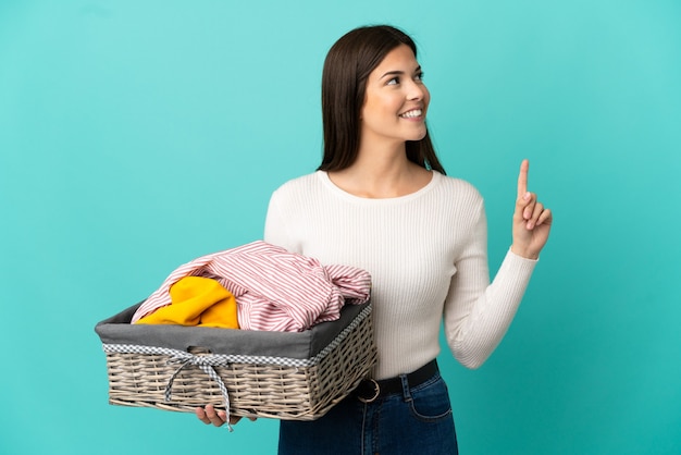 Adolescente ragazza brasiliana che tiene un cesto di vestiti isolato su sfondo blu che indica una grande idea