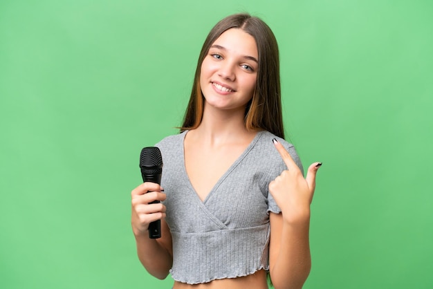 Adolescente ragazza cantante prelevando un microfono su sfondo isolato dando un pollice in alto gesto