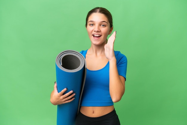 Adolescente ragazza caucasica andare a lezioni di yoga mentre si tiene un tappetino su sfondo isolato gridando con la bocca spalancata