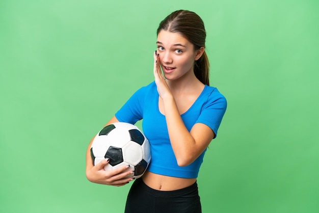 Adolescente ragazza caucasica che gioca a calcio su sfondo isolato sussurrando qualcosa