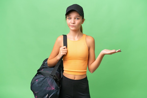 Adolescente ragazza caucasica con borsa sportiva su sfondo isolato facendo gesti di dubbi mentre si sollevano le spalle