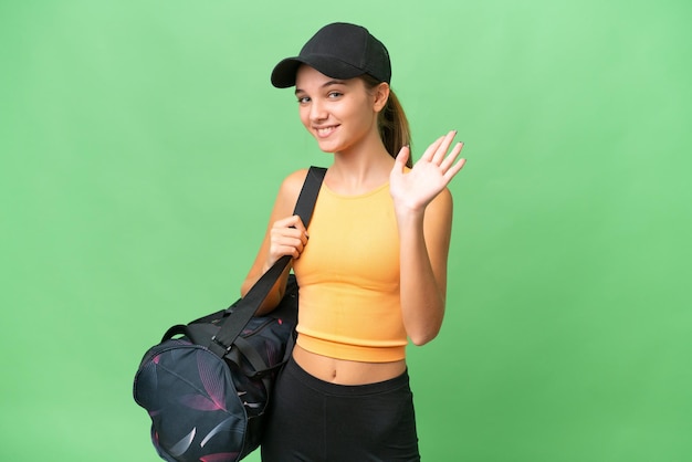 Adolescente ragazza caucasica con borsa sportiva su sfondo isolato salutando con la mano con felice espressione