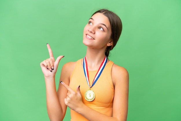 Adolescente ragazza caucasica con medaglie su sfondo isolato puntando con il dito indice una grande idea