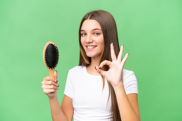 Adolescente ragazza caucasica con pettine per capelli su sfondo isolato che mostra segno ok con le dita