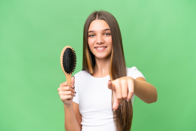 Adolescente ragazza caucasica con pettine per capelli su sfondo isolato punta il dito contro di te con un'espressione sicura