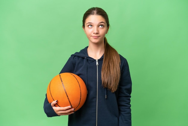 Adolescente ragazza caucasica giocare a basket su sfondo isolato e guardando in alto