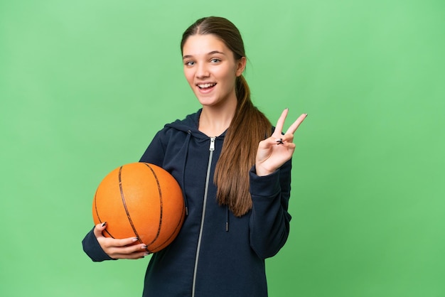 Adolescente ragazza caucasica giocare a basket su sfondo isolato sorridente e mostrando segno di vittoria