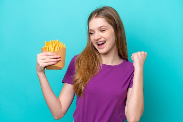 Adolescente ragazza russa che cattura patatine fritte isolate su sfondo blu che celebra una vittoria