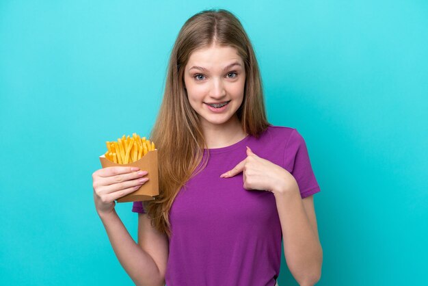 Adolescente ragazza russa che cattura patatine fritte isolate su sfondo blu con espressione facciale a sorpresa