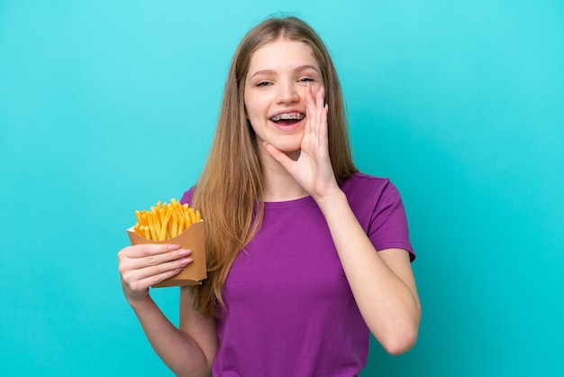 Adolescente ragazza russa che cattura patatine fritte isolate su sfondo blu gridando con la bocca spalancata