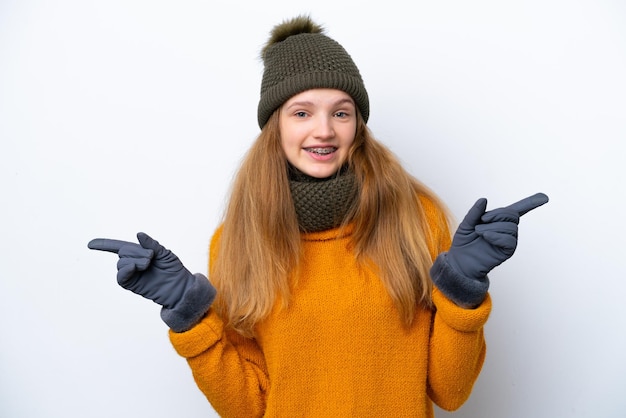 Adolescente ragazza russa che indossa una giacca invernale isolata su sfondo bianco che punta il dito verso i laterali e felice