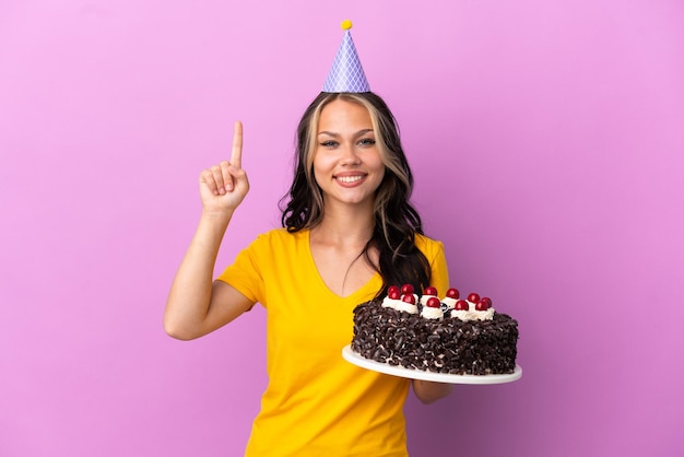 Adolescente ragazza russa con torta di compleanno isolata su sfondo viola che mostra e solleva un dito in segno del meglio