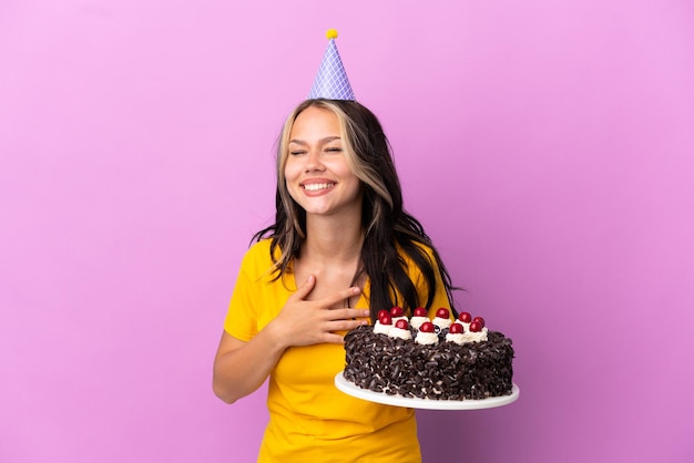 Adolescente ragazza russa con torta di compleanno isolata su sfondo viola sorridendo molto