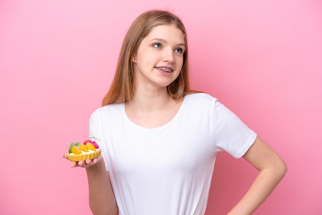 Adolescente ragazza russa in possesso di un tortino isolato su sfondo rosa in posa con le braccia all'anca e sorridente