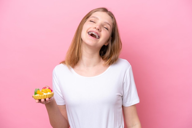 Adolescente ragazza russa in possesso di un tortino isolato su sfondo rosa ridendo