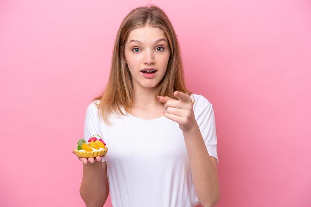 Adolescente ragazza russa in possesso di un tortino isolato su sfondo rosa sorpreso e puntato davanti