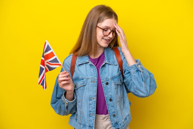 Adolescente ragazza russa in possesso di una bandiera del Regno Unito isolata su sfondo giallo ridendo