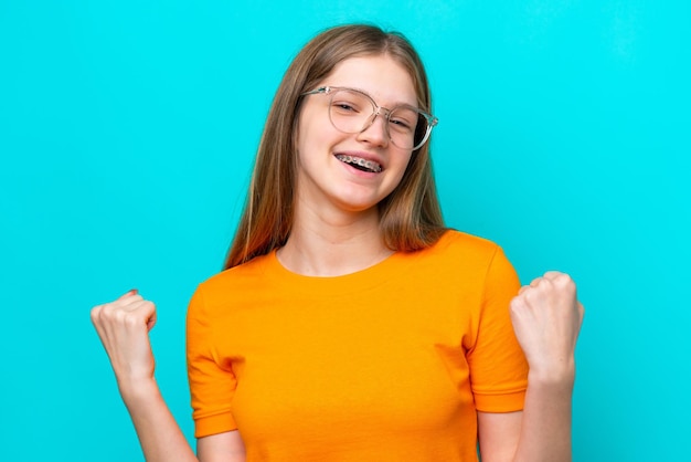 Adolescente ragazza russa isolata su sfondo blu Con gli occhiali e celebrare una vittoria