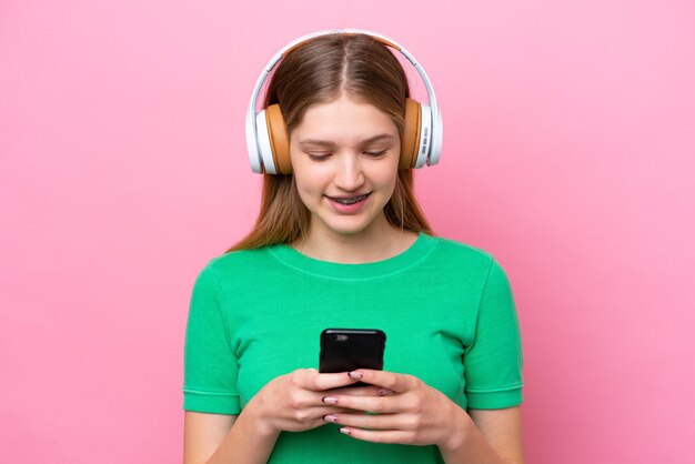 Adolescente ragazza russa isolata su sfondo rosa ascoltando musica e guardando al cellulare