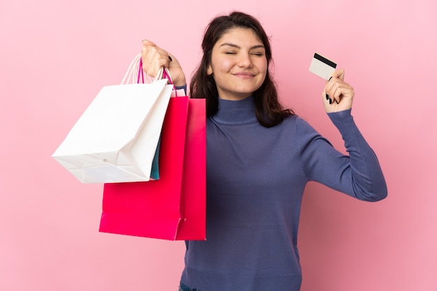 Adolescente ragazza russa isolata su sfondo rosa con borse della spesa e una carta di credito