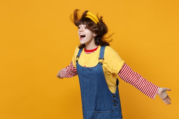 Adolescente ragazza urlante divertente in berretto francese con capelli svolazzanti che guardano da parte, allargando le mani isolate su sfondo giallo muro. Persone sincere emozioni, concetto di stile di vita. Mock up spazio di copia.