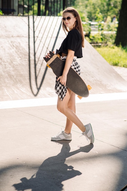 Adolescente skater ragazza in possesso di uno skateboard in piedi nel parco dei pattinatori
