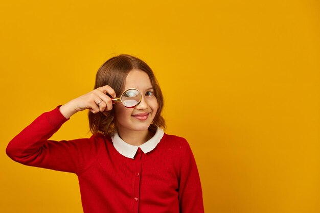 Adolescente sorridente alla moda della scuola che tiene la lente d'ingrandimento sul suo occhio