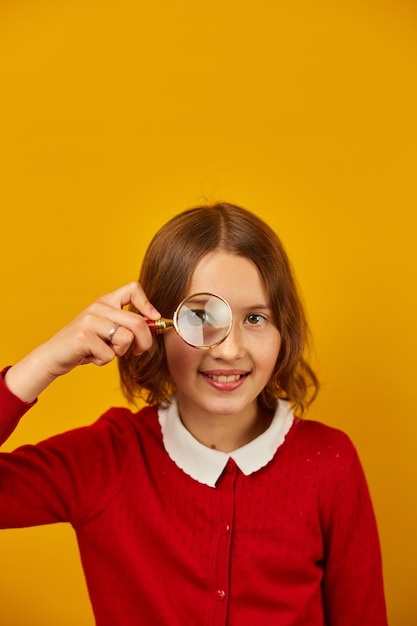 Adolescente sorridente alla moda della scuola che tiene la lente d'ingrandimento sul suo occhio