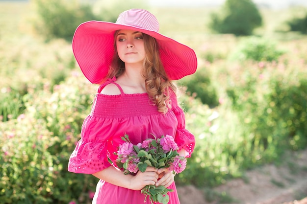 Adolescente sorridente che indossa un abito rosa e un cappello che tiene le rose