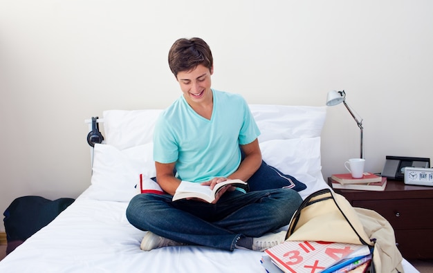 Adolescente sorridente che legge un libro nella sua camera da letto