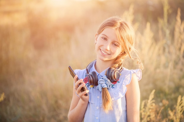 Adolescente sorridente con le cuffie che tengono lo smartphone in una mano sullo sfondo del campo di sole