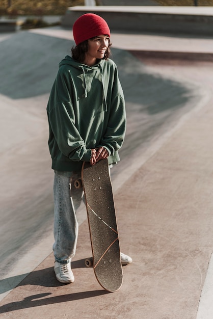 Adolescente sorridente con lo skateboard fuori allo skatepark