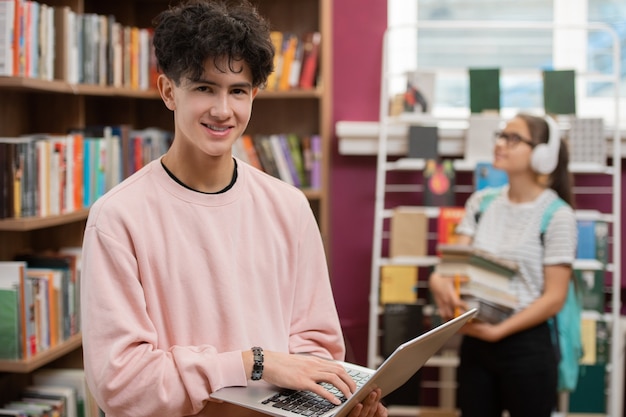 Adolescente sorridente in abbigliamento casual che tocca i tasti della tastiera del laptop mentre scorri l'elenco dei libri da leggere per gli esami