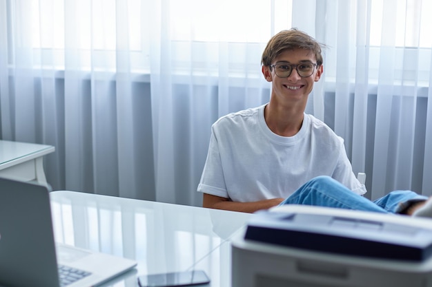 Adolescente sorridente sta lavorando o insegnando a casa con il suo laptop e smartphone