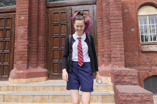 Adolescente studentessa in uniforme con zaino, sfondo della scuola di costruzione. Ritorno a scuola, ritorno al college, istruzione, concetto di adolescenti