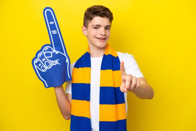 Adolescente tifoso sportivo uomo isolato su sfondo giallo che mostra e alza un dito