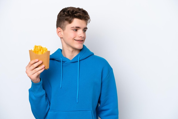 Adolescente uomo russo azienda patate fritte isolate su sfondo bianco guardando al lato e sorridente