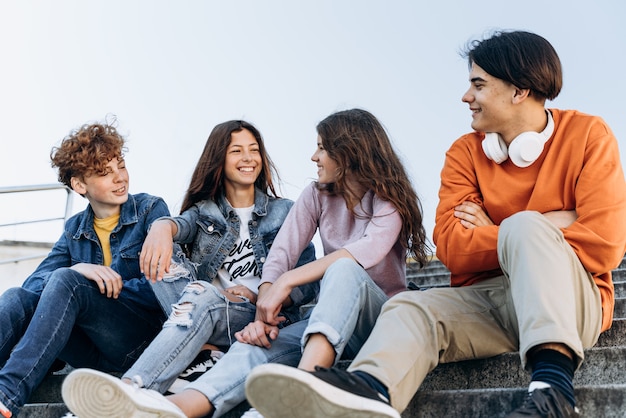 Adolescenti belli e positivi comunicano felicemente tra loro all'aperto. Gli adolescenti si siedono su una panchina e parlano.